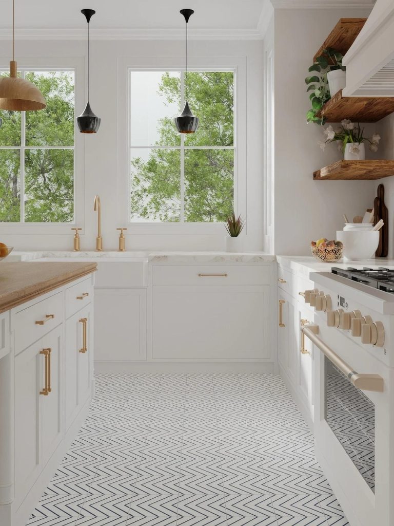 A bright, modern kitchen featuring white cabinetry with gold hardware, a chevron-patterned floor, black pendant lights, and large windows overlooking green trees.